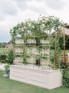 an outdoor wedding venue with white flowers and greenery on the wall, surrounded by wine glasses