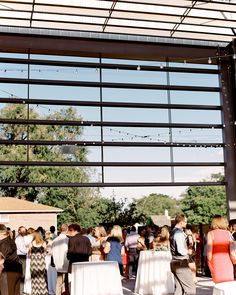 a group of people standing around tables in front of an open air structure with lots of windows