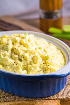 a blue bowl filled with mashed potatoes on top of a wooden table next to sliced celery