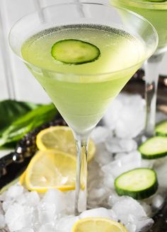 two glasses filled with cucumber and lemonade on top of ice cubes