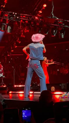 two people on stage with microphones in front of them and one person wearing a pink hat