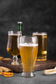 three glasses filled with beer sitting on top of a wooden tray next to crackers