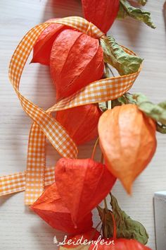 some red and orange flowers are on a white table with gingham ribbon around them