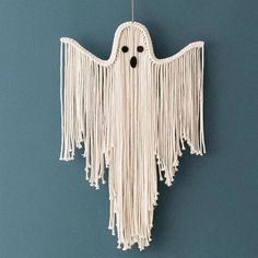 a white hanging decoration with fringes and eyes on it's face, in the shape of a ghost