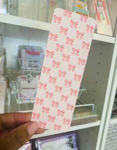 a person holding up a piece of paper with pink bows on it in front of a book shelf