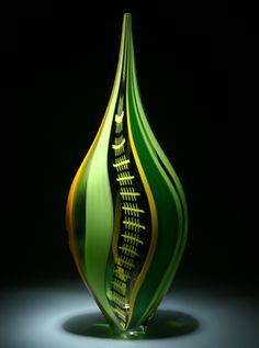 a green and yellow vase sitting on top of a black table next to a wall