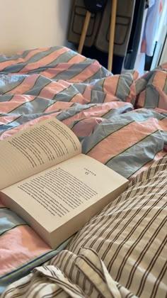 an open book sitting on top of a bed next to a pillow and blanket in a bedroom