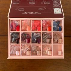 an open pink box filled with lots of different colored nail polishes on top of a wooden table