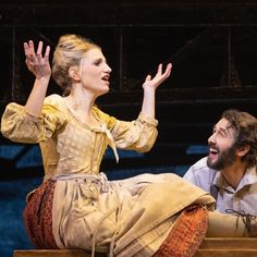 a man sitting next to a woman on top of a wooden bench with their hands in the air