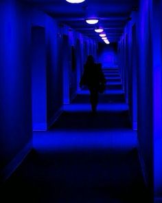 a person walking down a dark hallway with blue lights on either side of the corridor