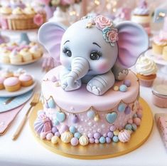 an elephant figurine sitting on top of a pink and blue cake surrounded by cupcakes