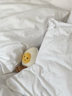 a stuffed animal is peeking out from under the covers in an unmade bed with white sheets