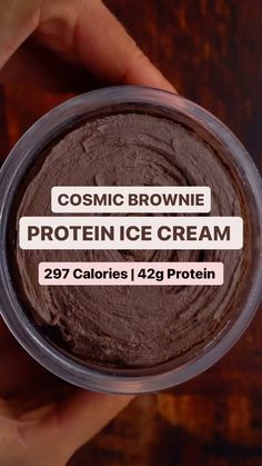 someone holding up a container of protein ice cream on a wooden table with the text cosmic brownie protein ice cream