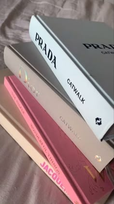 three books stacked on top of each other in front of a white bed sheet with pink lettering