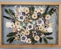 an arrangement of flowers and seashells in a wooden frame with sea shells on the bottom