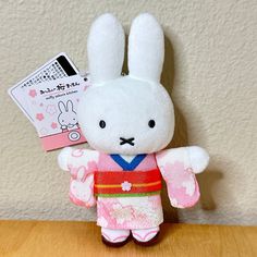 a small stuffed rabbit is wearing a kimono and standing on a wooden table next to a wall