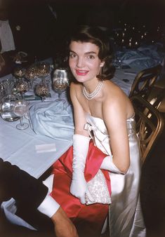 a woman sitting at a dinner table in a red and white dress with gloves on