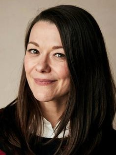 a woman with long dark hair wearing a red and black sweater smiles at the camera