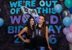 two young women standing in front of a backdrop with balloons and streamers that say we're out of this world birthday