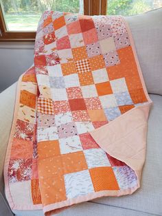 an orange and white patchwork quilt sitting on a couch in front of a window