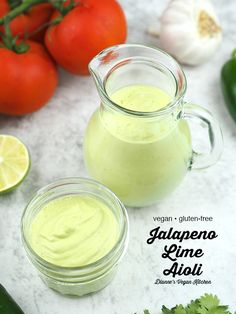 two small jars filled with green liquid next to tomatoes and cucumbers on a table