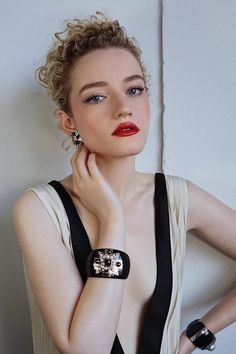 a woman with her hand on her chin wearing a black and white dress, red lipstick and bracelet