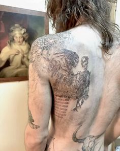 the back of a man with tattoos on his upper and lower half, standing in front of a painting