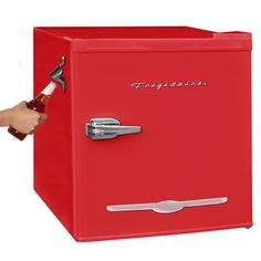 a red refrigerator with a bottle opener on the door and a hand holding a wrench