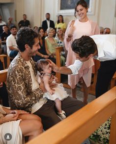 a group of people sitting and standing around each other in a room with wooden pews