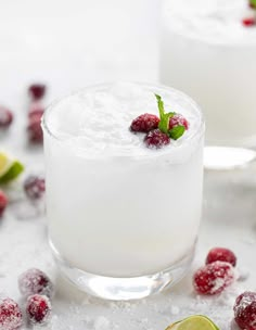 two glasses filled with ice and raspberries on top of a white table next to limes