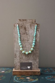 a necklace with turquoise beads is on display in front of a paper bag that has a tag attached to it