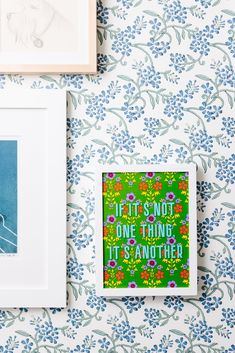 two framed pictures hang on the wall next to a blue flowered wallpaper with an art print