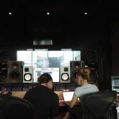 two people are sitting in front of sound equipment and looking at something on the computer screen