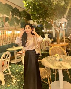 a woman in a long black skirt standing next to a table with chairs and tables