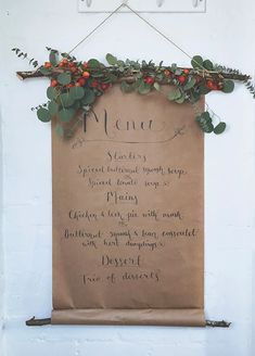 a menu hanging on the side of a white wall with greenery and berries attached to it