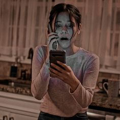 a woman with makeup on her face is looking at a cell phone in the kitchen