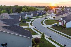 an aerial view of houses in a neighborhood with the sun setting over the trees and grass