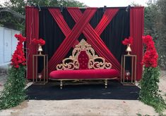 a red and gold stage set up with flowers on the side for a wedding ceremony