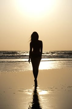 a woman walking on the beach at sunset