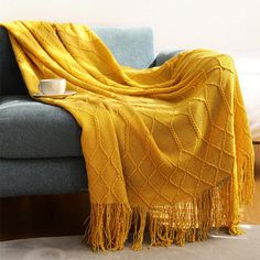 a couch with a yellow blanket on top of it next to a coffee cup and saucer