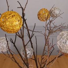 a vase filled with gold and silver balls on top of a wooden table next to a tree