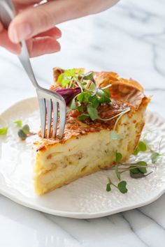 a person is holding a fork over a piece of quiche on a white plate