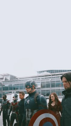 a group of people standing next to each other in front of a building with captain america on it