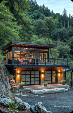 a modern house in the woods with lights on and stairs leading up to it's second floor