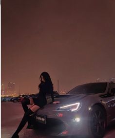 a woman sitting on top of a car in front of a city skyline at night