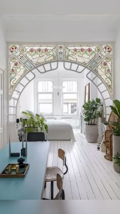 a bedroom with white walls and stained glass window above the bed, along with potted plants