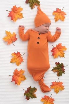 a baby in an orange outfit surrounded by autumn leaves