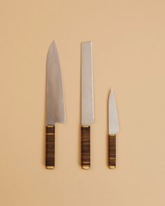 three knives are sitting next to each other on a beige surface with gold trimmings