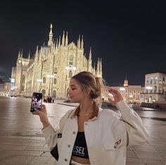 a woman taking a selfie in front of a cathedral at night with her cell phone