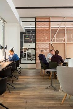 people are sitting at desks in an office with glass walls and wood flooring